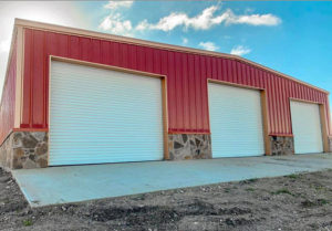 Large commercial building with three white garage doors and slab of concrete.