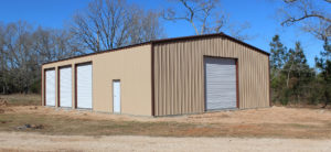 Beige metal building with four visible overhead garage doors. Blue skies in background.